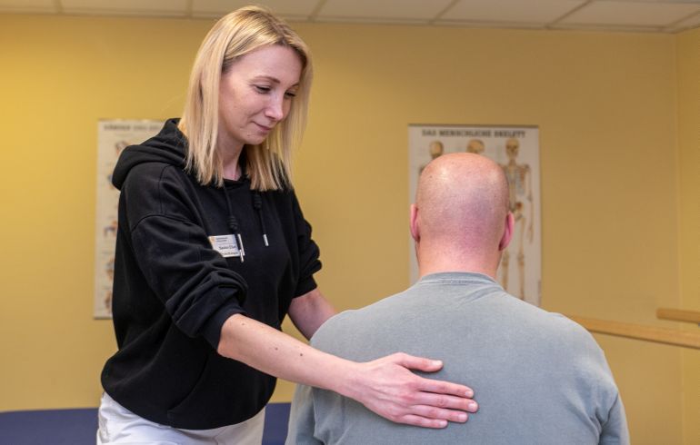 Eine Mitarbeiterin der Physiotherapie der SBK legt ihre Hand auf den Rücken eines Patienten.