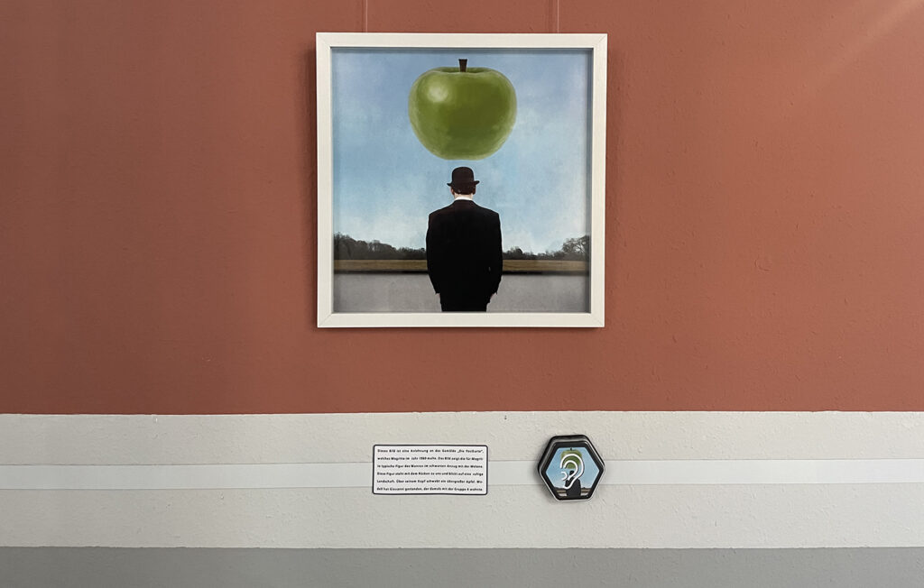 Ein Bild der Ausstellung "Aus Liebe zu Magritte". Darunter die Bildbeschreibung und ein Talkerbutton.