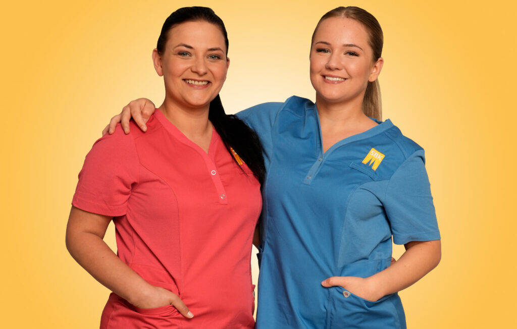 Zwei Auszubildende in SBK-Dienstkleidung lächeln Arm in Arm in die Kamera.